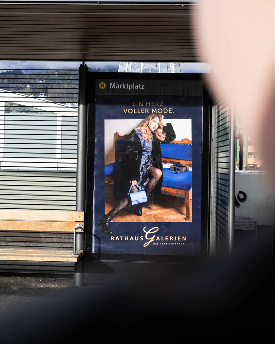rathausgalerien innsbruck winterkampagne citylights frau auf blauer bank mit langem mantel als citylight plakat am marktplatz in innbruck